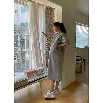 淺灰色寬鬆連身裙，圓領短袖設計，模特側身持書站立於落地窗與書堆前｜圓領素色側開衩連身裙（第 310 張）