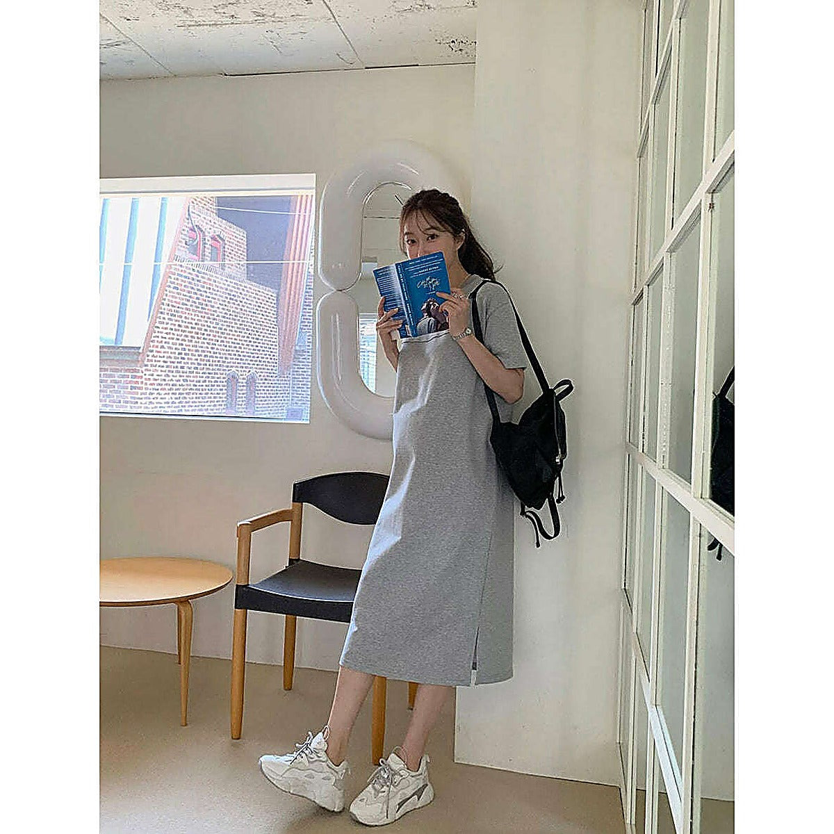 淺灰色連身裙正面全身視角，圓領短袖及膝長度，模特持書站立於窗邊椅旁｜圓領素色側開衩連身裙（第 318 張）