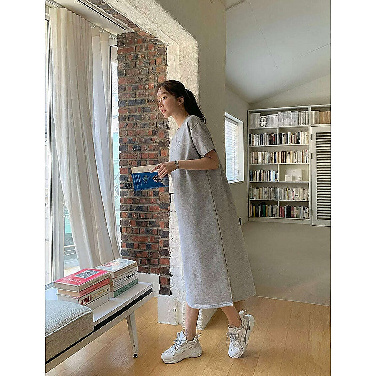模特兒實穿淺灰短袖連身裙（側開衩），窗邊全身、手持藍色書本｜圓領素色側開衩連身裙（第 2 張）